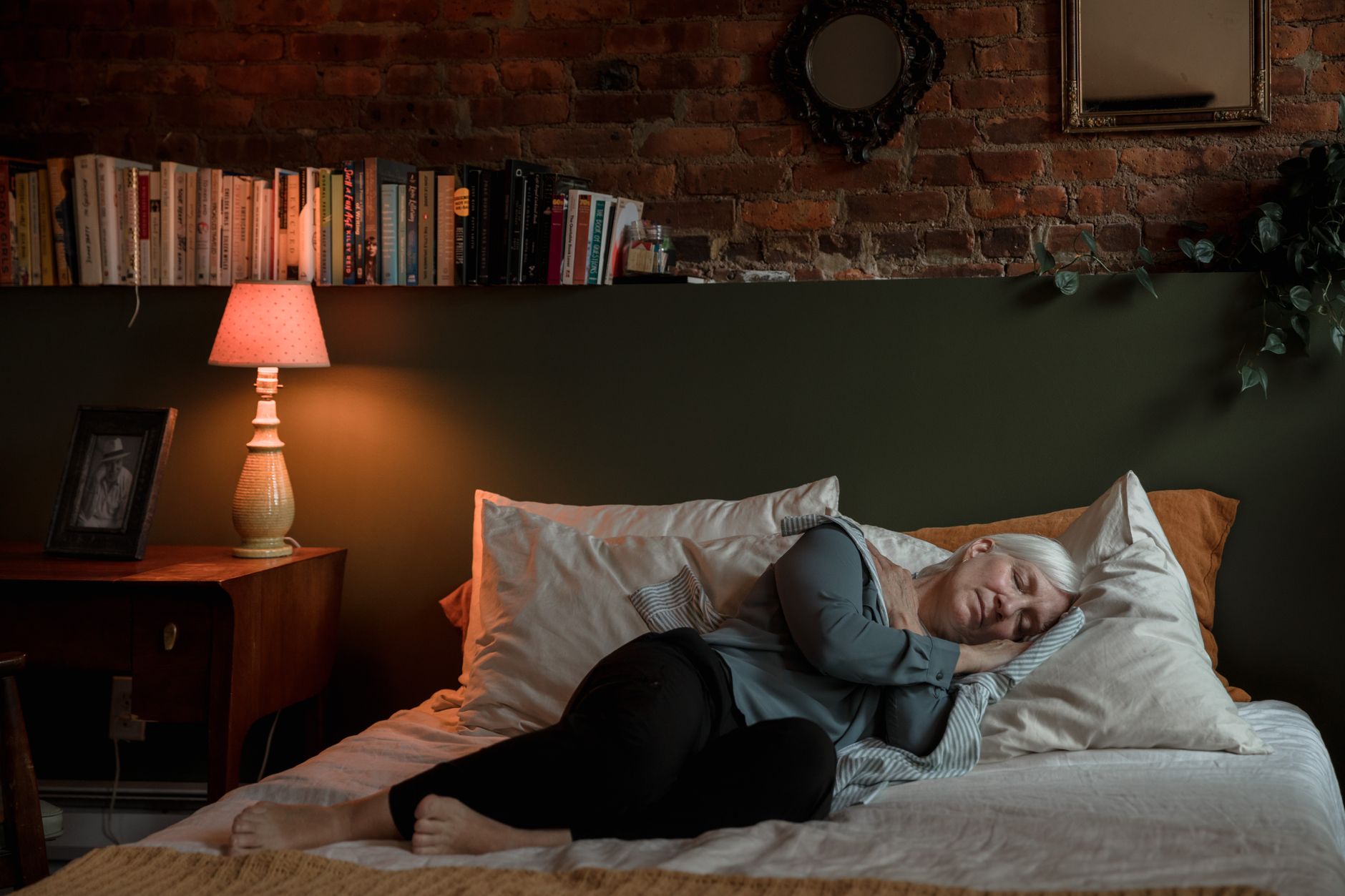 Femme allongée sur le côté dans son lit, genoux fléchis et jambes superposées, position concernée par le coussin entre les genoux