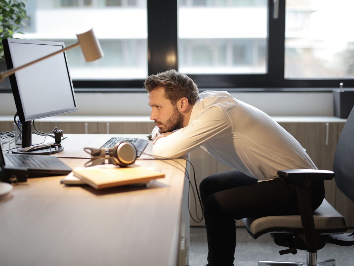 Homme fatigué affaissé sur son bureau face à son écran, illustrant les conséquences d'une mauvaise posture